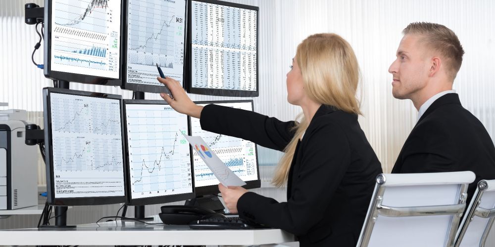 two office workers stare at six computer screens