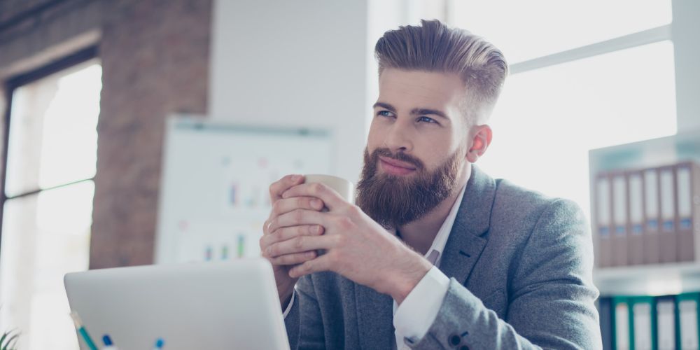 happy, dreamy young male office worker with coffe and laptop